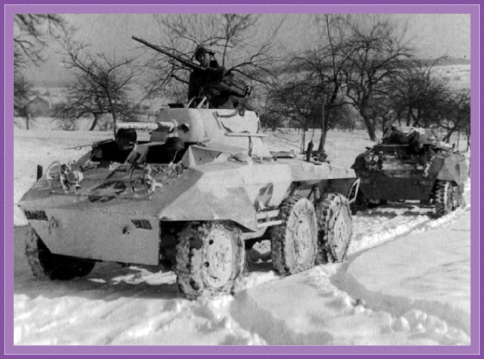 Two M8 Greyhounds, one with a winter whitewash, travel through the Ardennes Forest during the Battle of the Bulge December 1944 – January 1945.